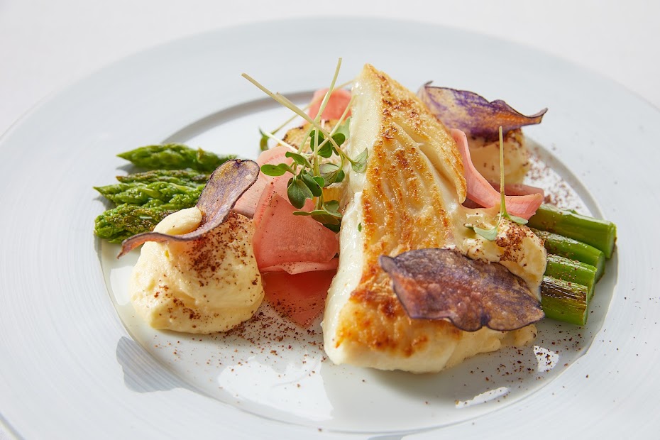 Gebratenes Fischfilet mit grünem Spargel und Kartoffelchips auf weißem Teller – frischer Fischgenuss im Weinforum Franken