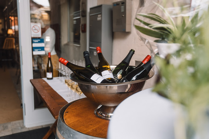 Weinflaschen im Sektkühler auf Weinfass vor dem Eingang der Vinothek